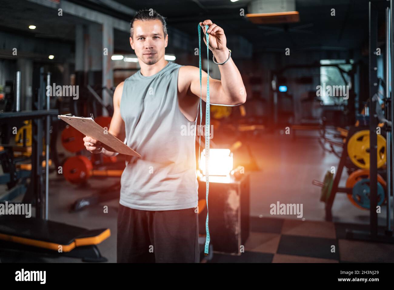 young handsome personal trainer nutritionist with measuring tape in gym Stock Photo