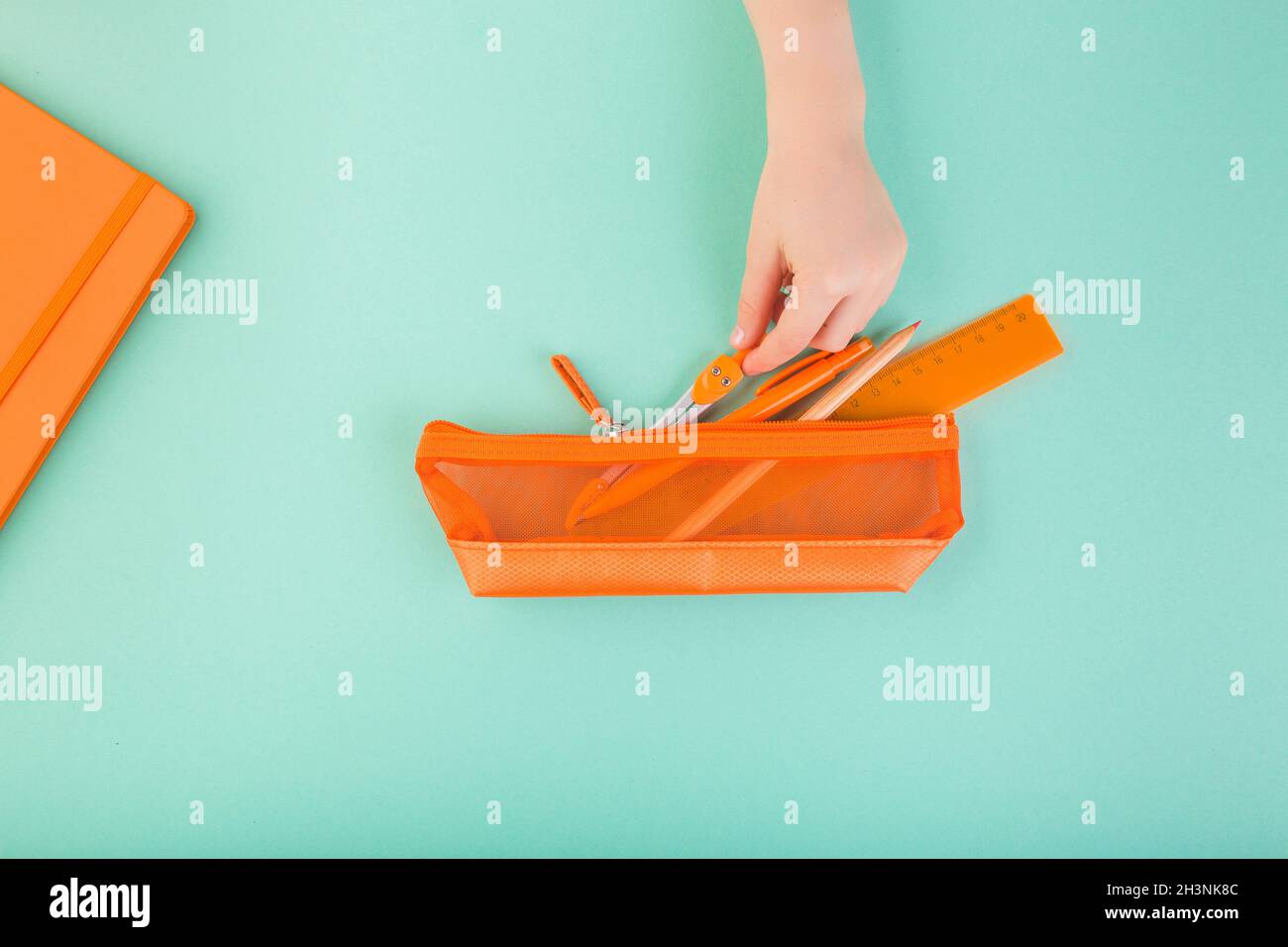Child's hand keeping all the pencils, pens, scissors, etc. in orange pencil case. Back to school concept Stock Photo