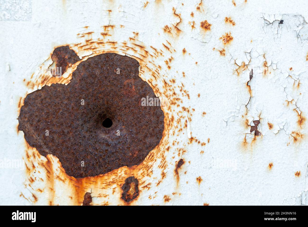 Firearm bullet hole in white painted sheet metal. Natural aging of the metal. Rust. Stock Photo