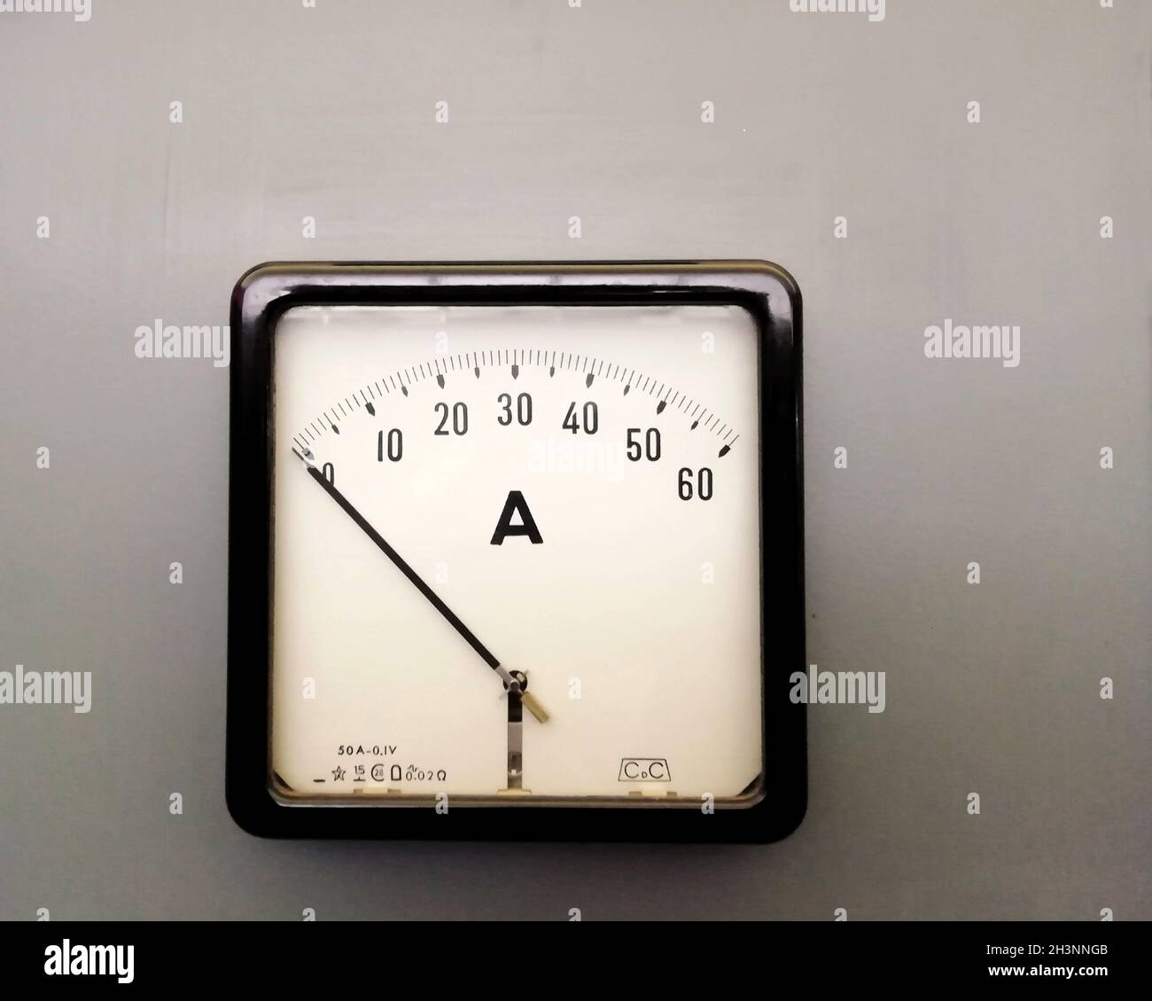 A large square industrial ammeter with an analogue dial with numbers with standard electrical symbols on a white dial on a grey Stock Photo