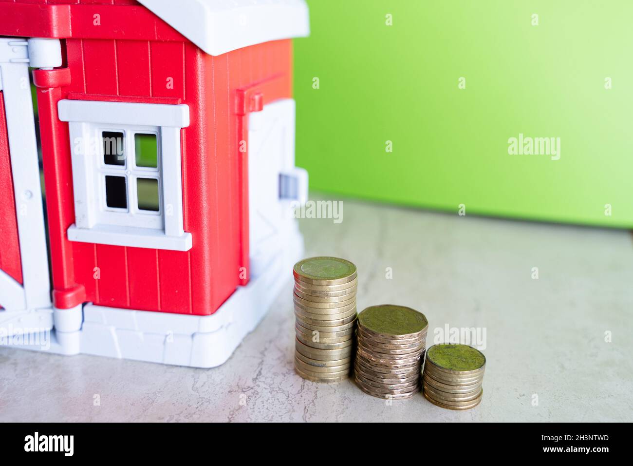 Coin ladder by red house miniature over green background. Savings, down payment mortgage, real estate market concepts Stock Photo