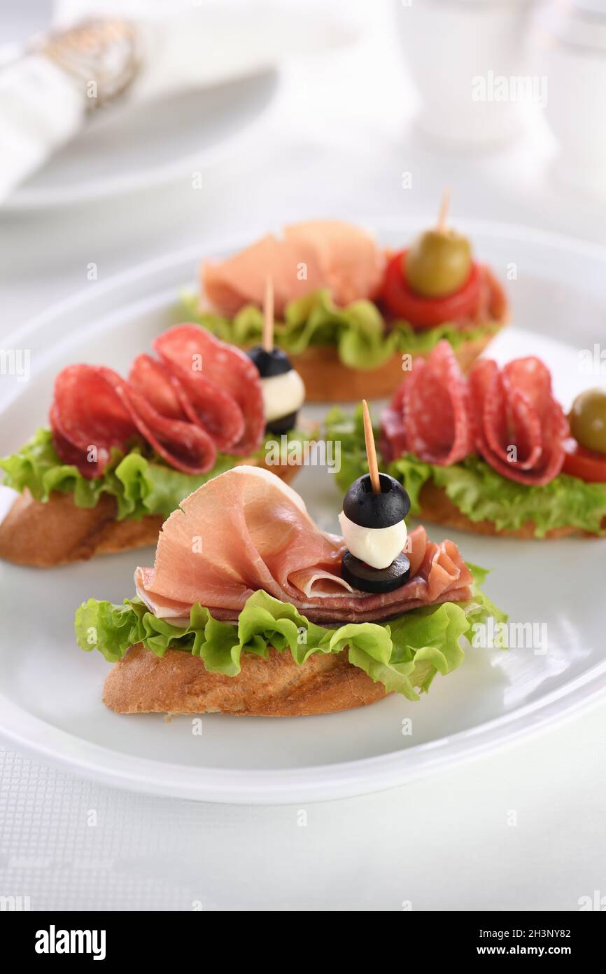 Tender baguette canapes with Leaf lettuce, salami or Parma ham, tomatoes,  mozzarella and olive. Deli Stock Photo - Alamy