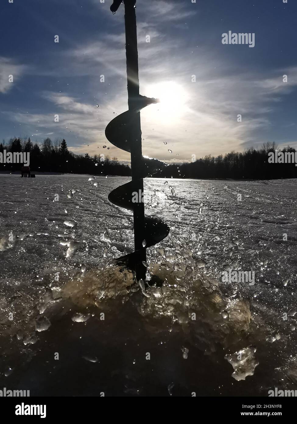 Drilling a hole into the thick ice for fishing in Finland Stock Photo