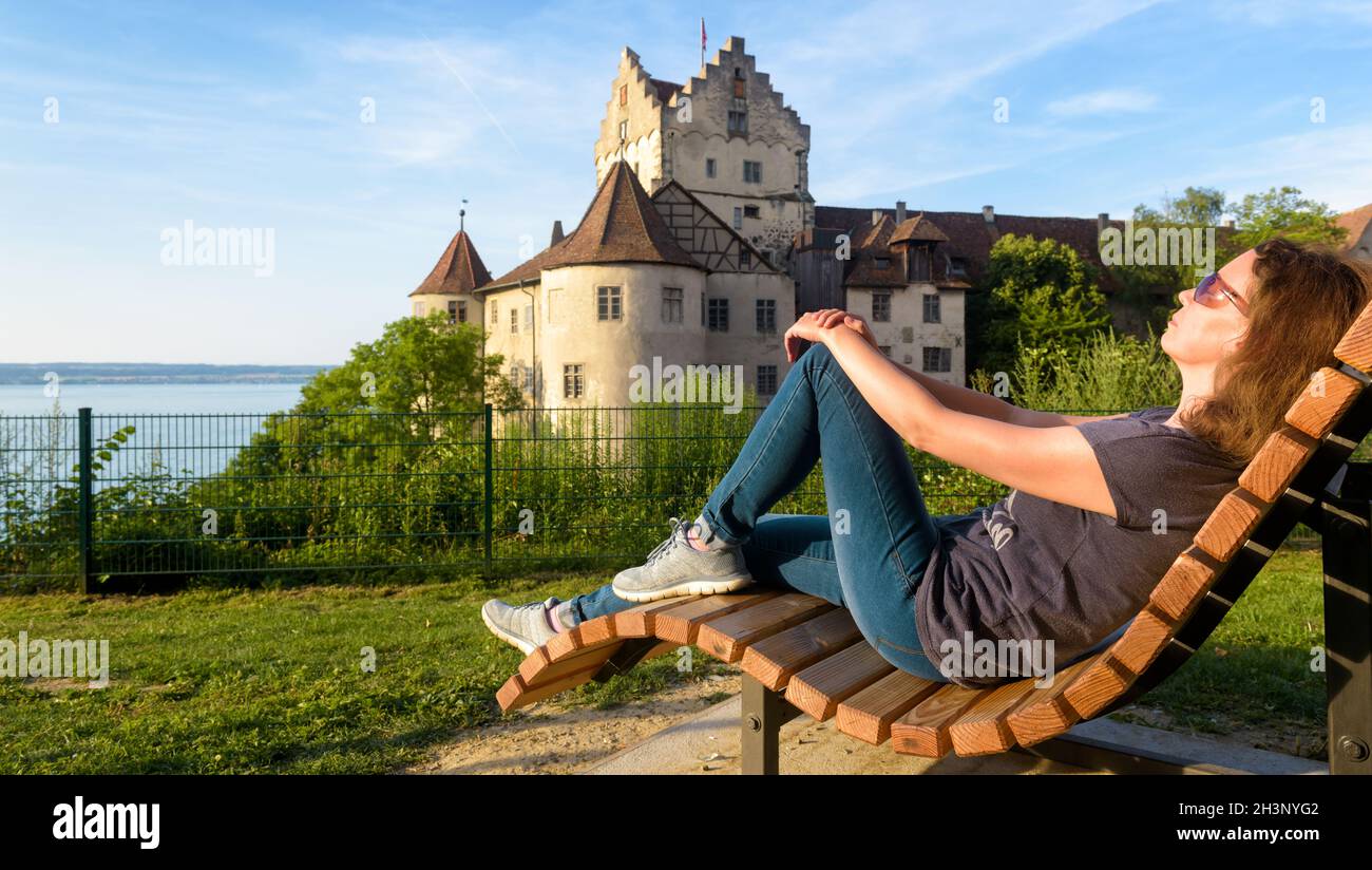 Adult girl tourist rests at Meersburg Castle overlooking Lake Constance (Bodensee) in summer, Germany, Europe. Young woman sunbathes near Swabian land Stock Photo