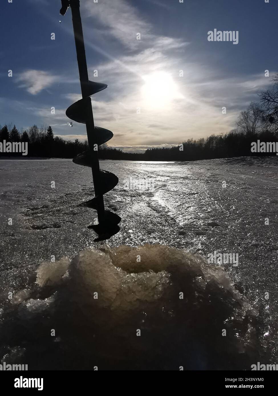 Drilling a hole into the thick ice for fishing in Finland Stock Photo