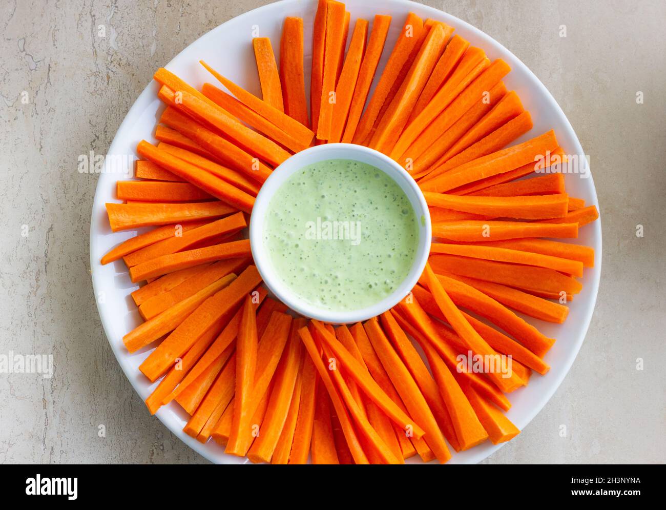 Carrot sticks plate with green sauce dip in the middle. Healthy, vegetarian snack concept Stock