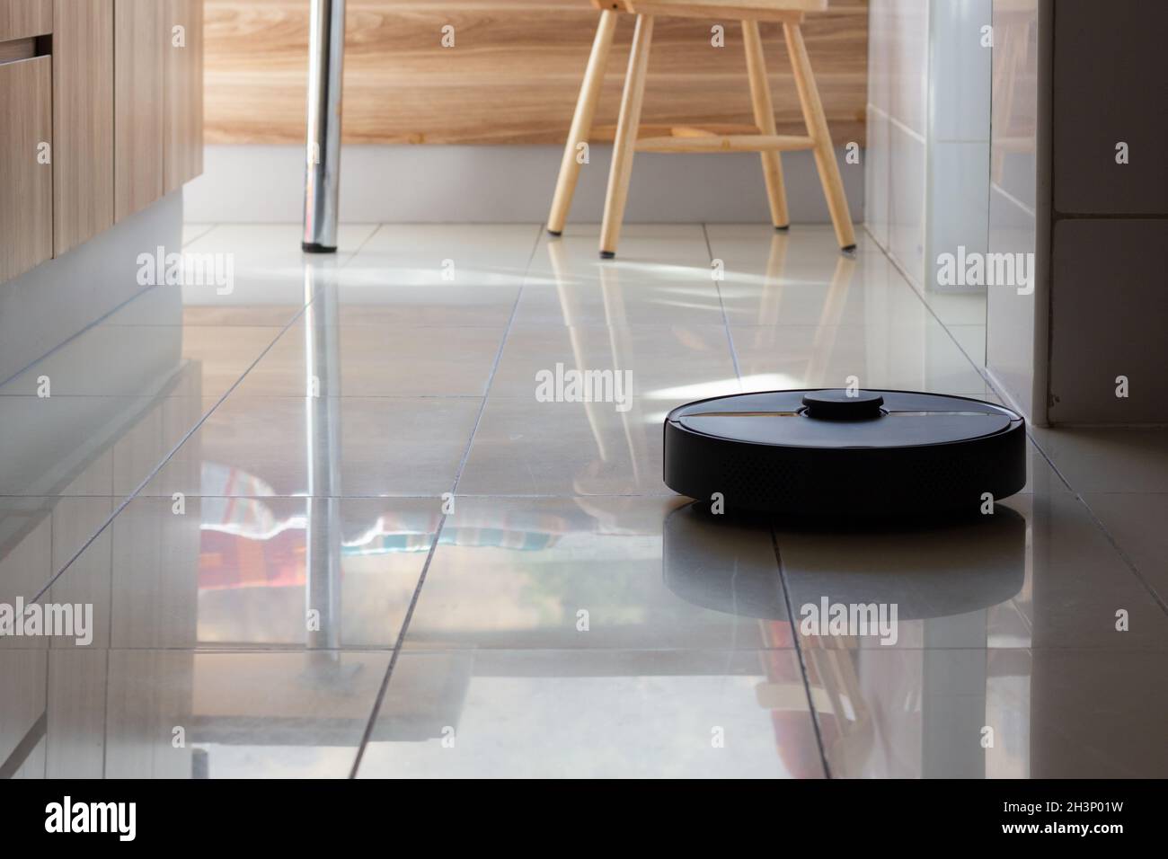 Robot vacuum cleaner working on kitchen floor. Automated smart machine