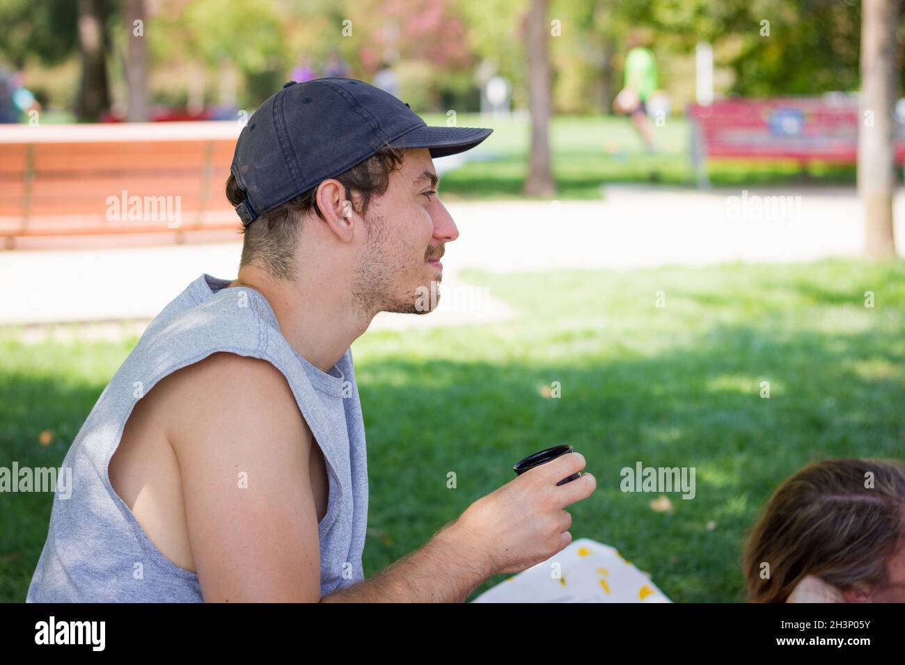 Smiling young man with cap holding drink in park. Leisure time outdoors concept Stock Photo