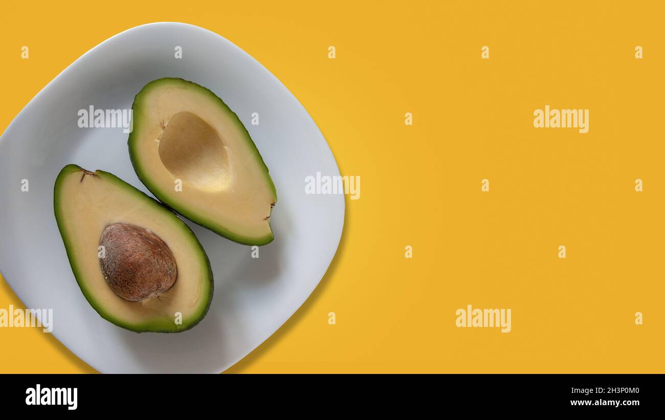 Two parts of avocado on white plate. Isolated on yellow background. 16x9 size. Template for banner with copy space at right side Stock Photo