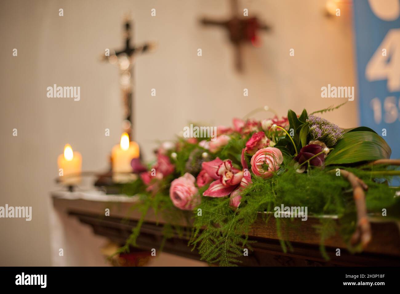 Interior of a Roman Catholic Church with polychrome decoration of the altar and flowers, with an out of focus cross with Jesus C Stock Photo