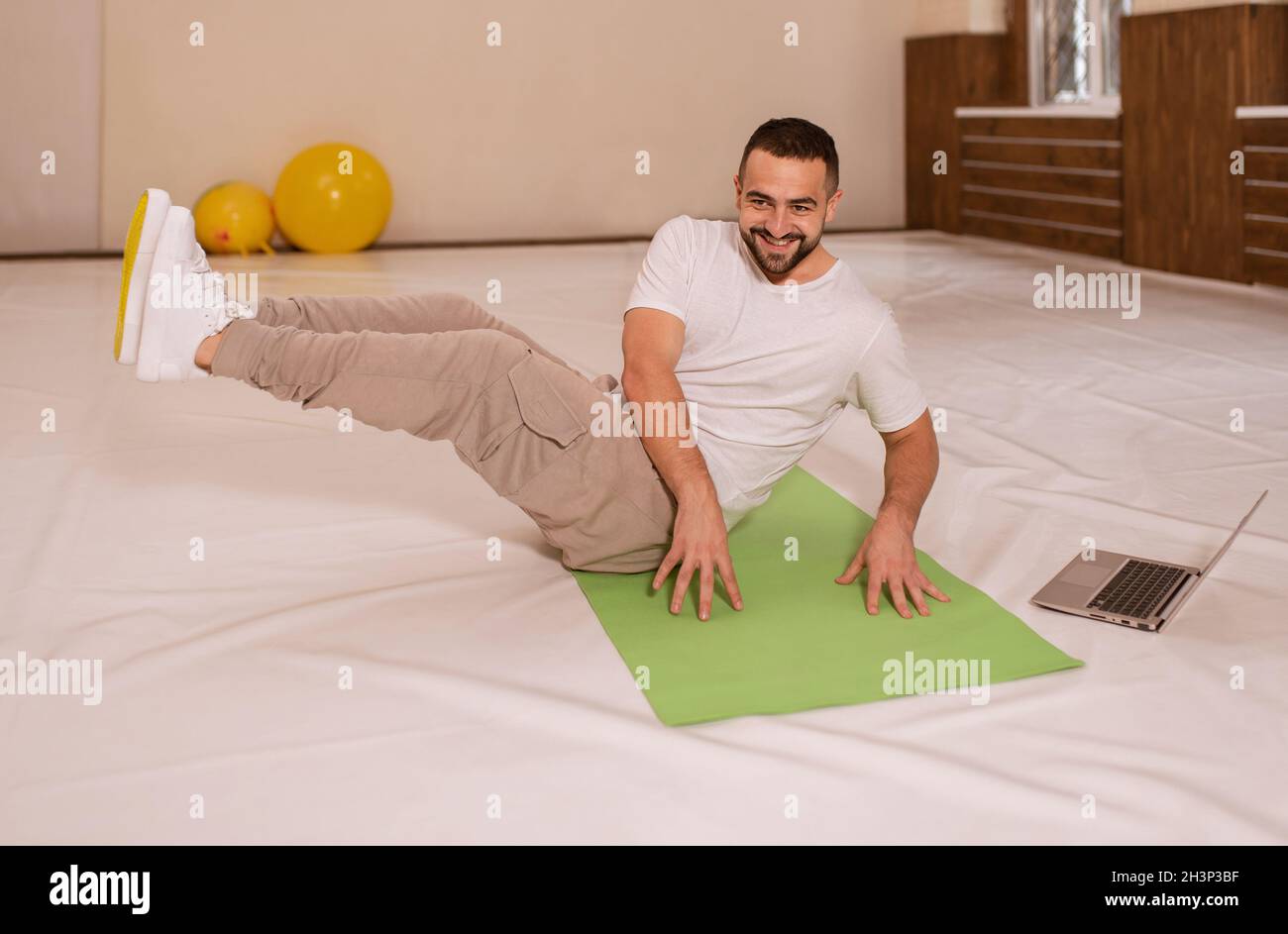 High top angle. Young handsome man doing crunches abs core looking at camera while playing online work out videos on using lapto Stock Photo