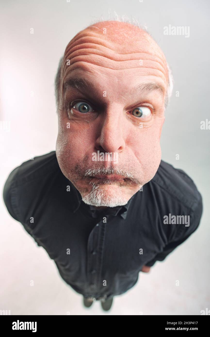 Senior man pulling a funny or comic face in a top down view as he looks up at the camera with bulging eyes and puffed out red cheeks while biting his Stock Photo
