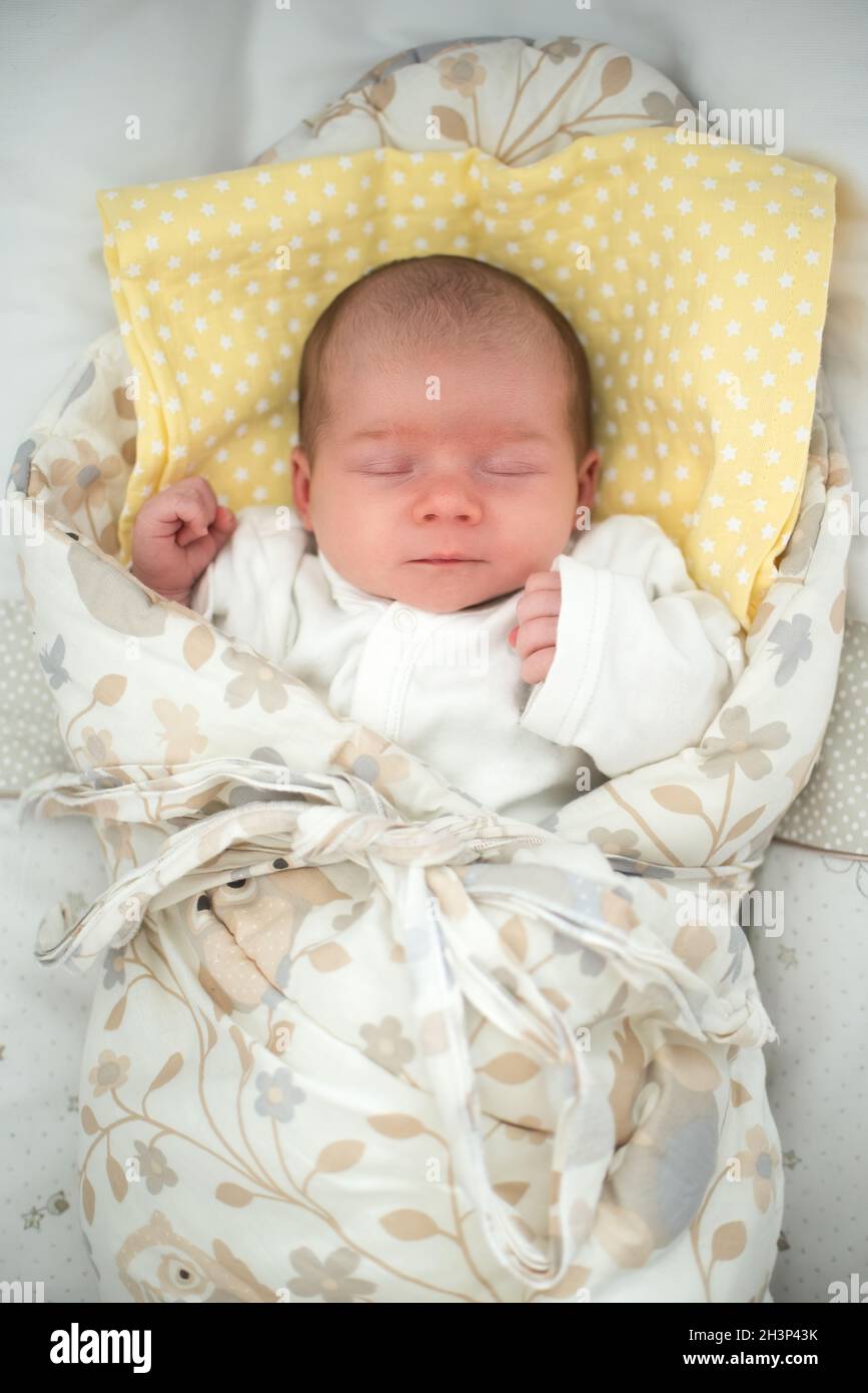 Cute newborn baby sleeping in swaddle wrap with smile on her face Stock