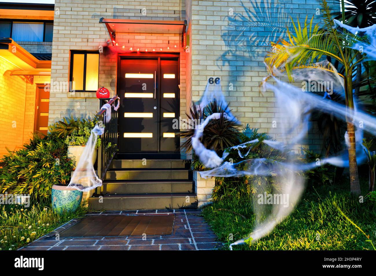 Witch and pumpkin scarry face with lights and spider webs around house from entrance and front yard at night - halloween. Stock Photo