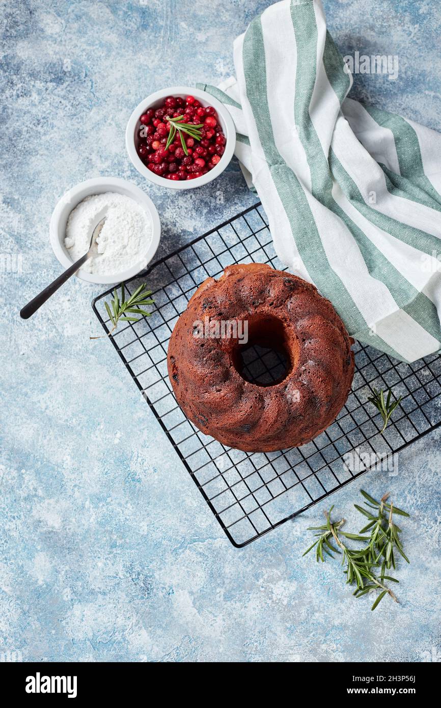 Chocolate bundt cake on a metal wire rack, powdered sugar and cranberries in bowls Stock Photo