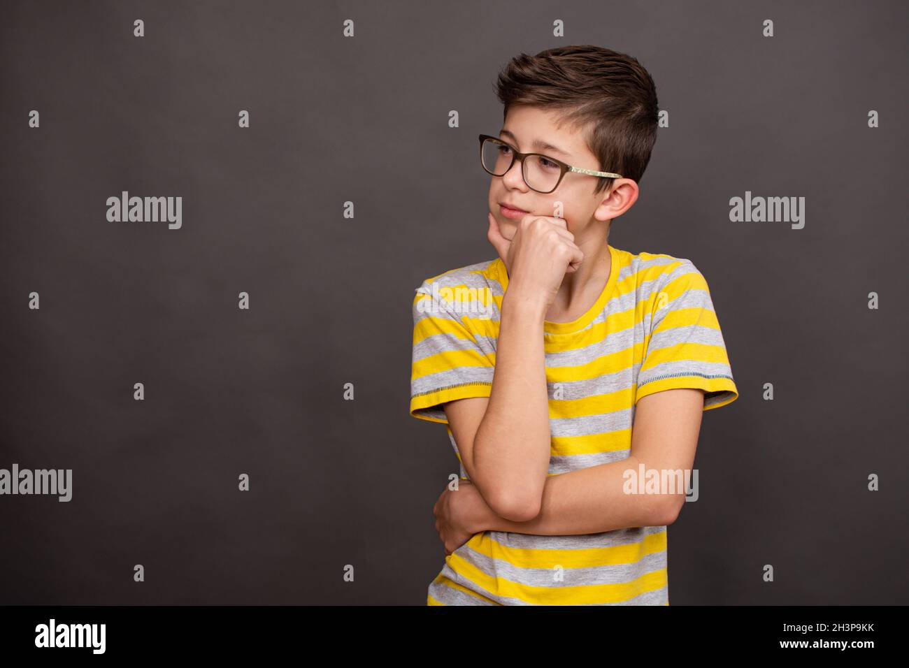 A teenage boy thought about it. Serious face. Isolated over dark grey background, copy space. Stock Photo