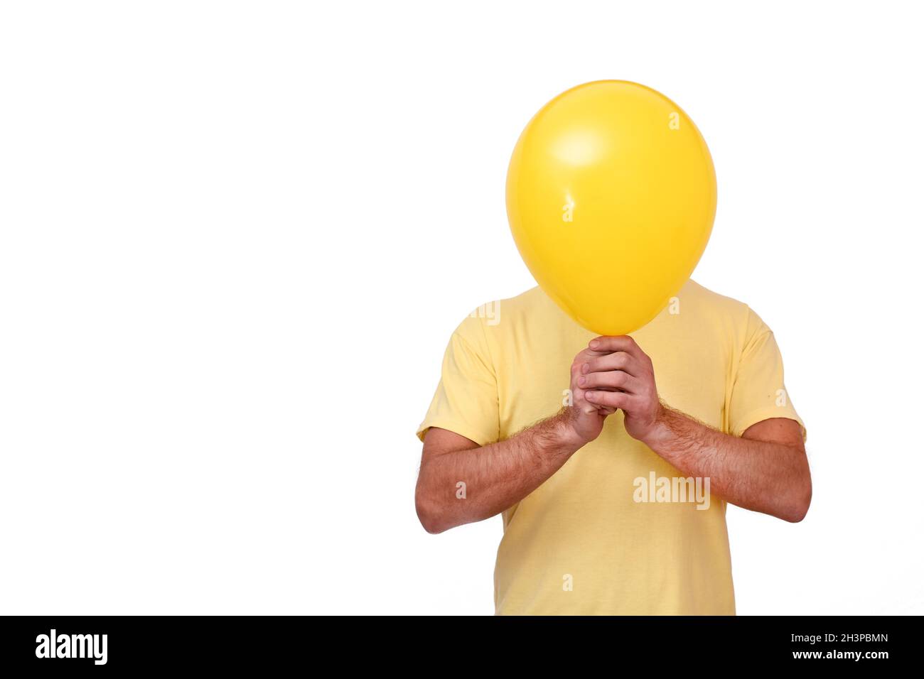 A man holds a balloon in front of him. Yellow ball covering the face. Stock Photo