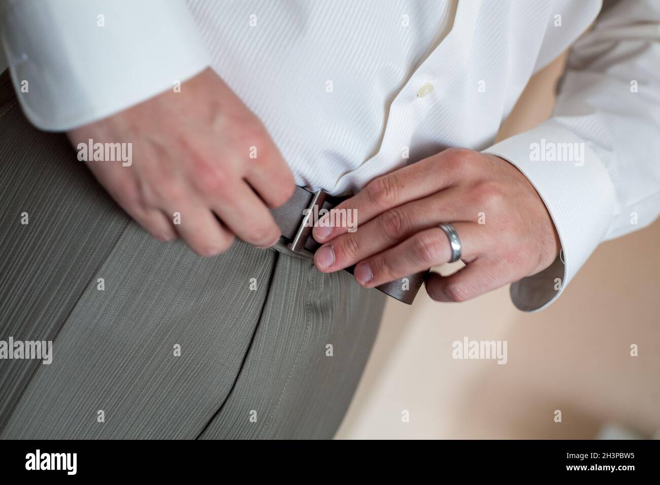 A man in pants and shirt buttoned a black leather trouser belt. Groom Dress up a belt with buckle. Businessman wear leather styl Stock Photo