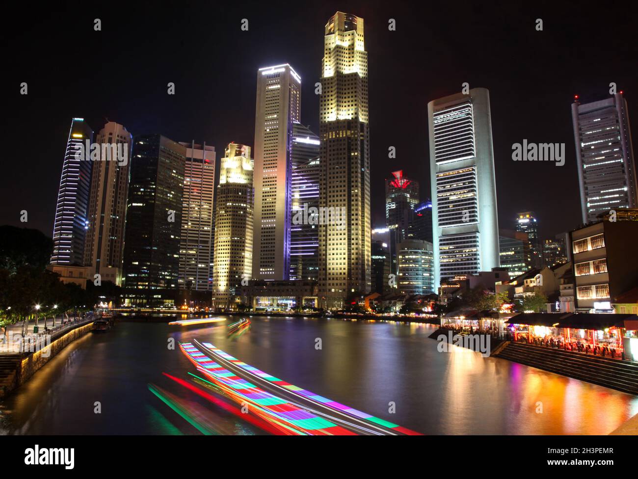 Night time in Singapore at South Bridge Road showing illuminated buildings and light trail from tourist boats cruising the Singapore river. Stock Photo