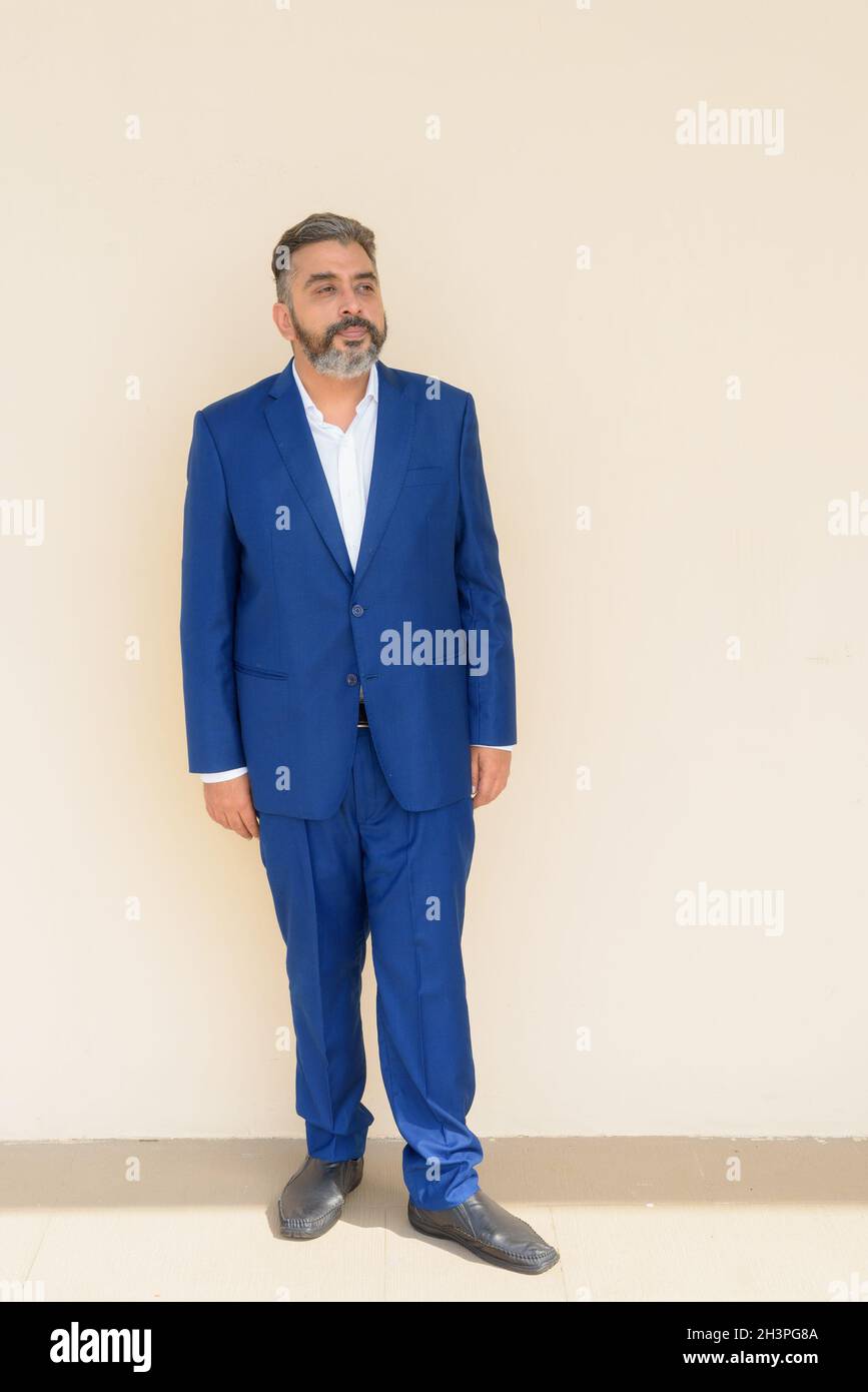 Full length portrait of handsome bearded Indian businessman against plain background Stock Photo