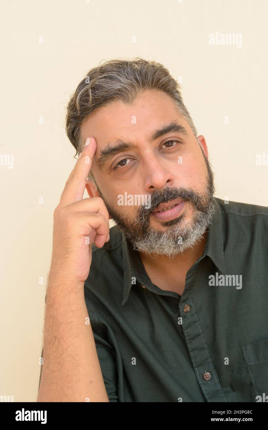 Portrait of handsome bearded Indian businessman against plain background Stock Photo