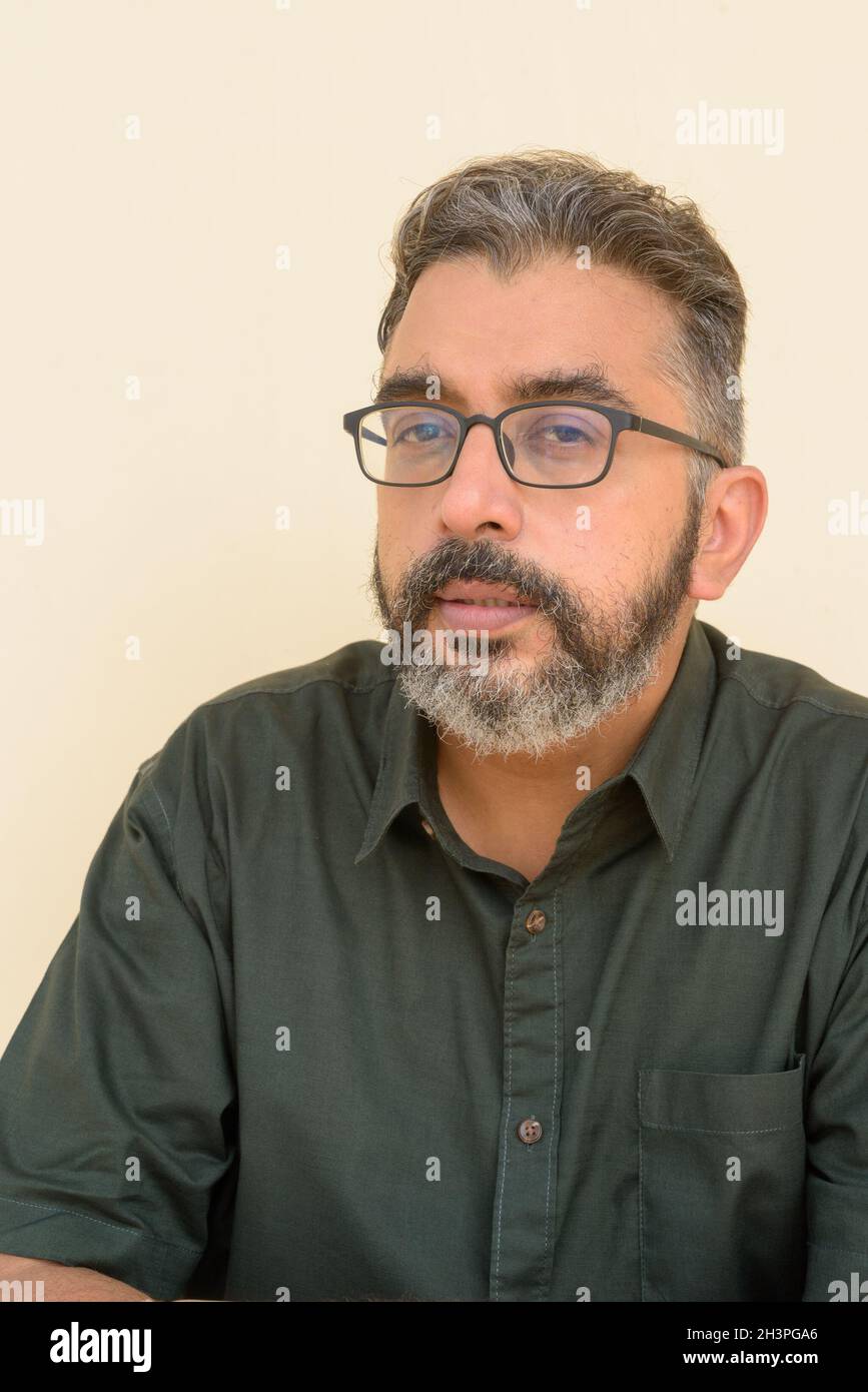 Portrait of handsome bearded Indian businessman against plain background Stock Photo
