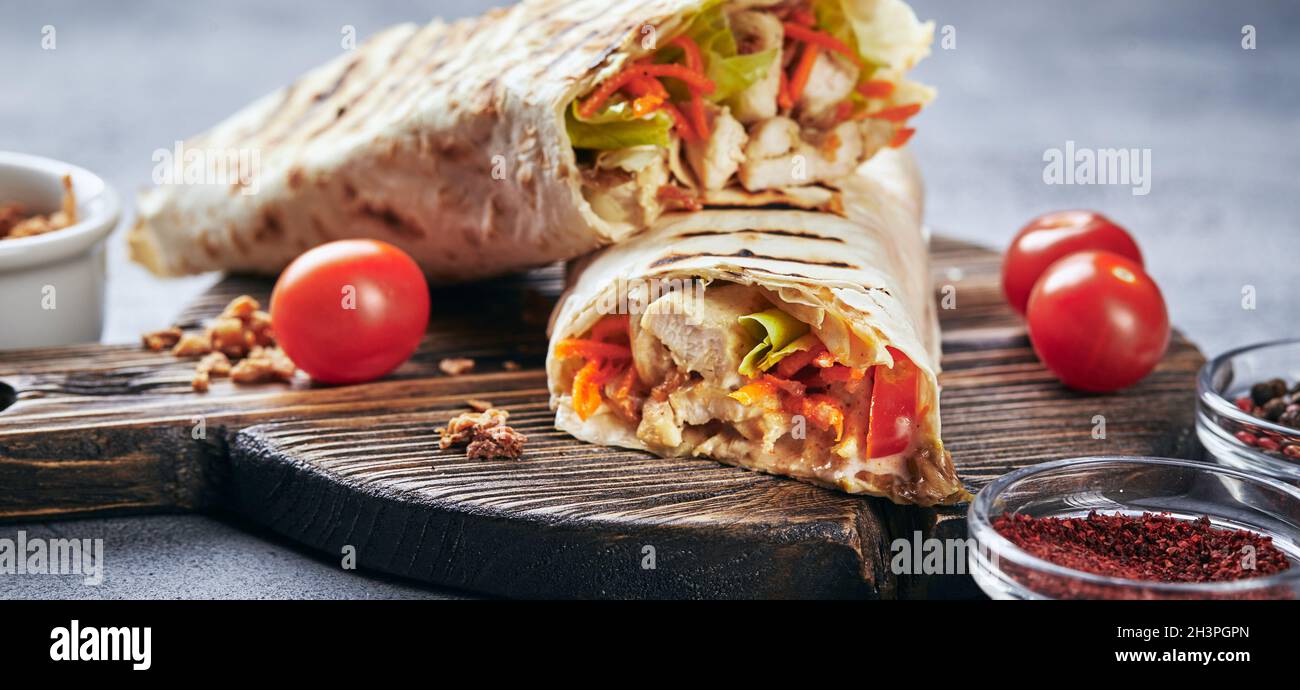 Eastern traditional shawarma with chicken and vegetables, Doner Kebab with sauces on wooden cutting board. Stock Photo