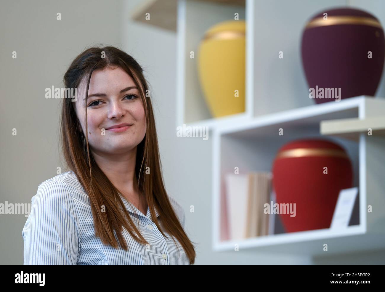 Leipzig, Germany. 18th Oct, 2021. Paula Meißner stands in front of various urns in a consultation room at Ananke Funerals. As a prospective office administrator, Paula is in her second year of training at the funeral home. According to industry sources, funeral homes have no problems finding young talent. (to dpa 'Popular profession: funeral homes have no worries about finding new recruits') Credit: Hendrik Schmidt/dpa-Zentralbild/dpa/Alamy Live News Stock Photo