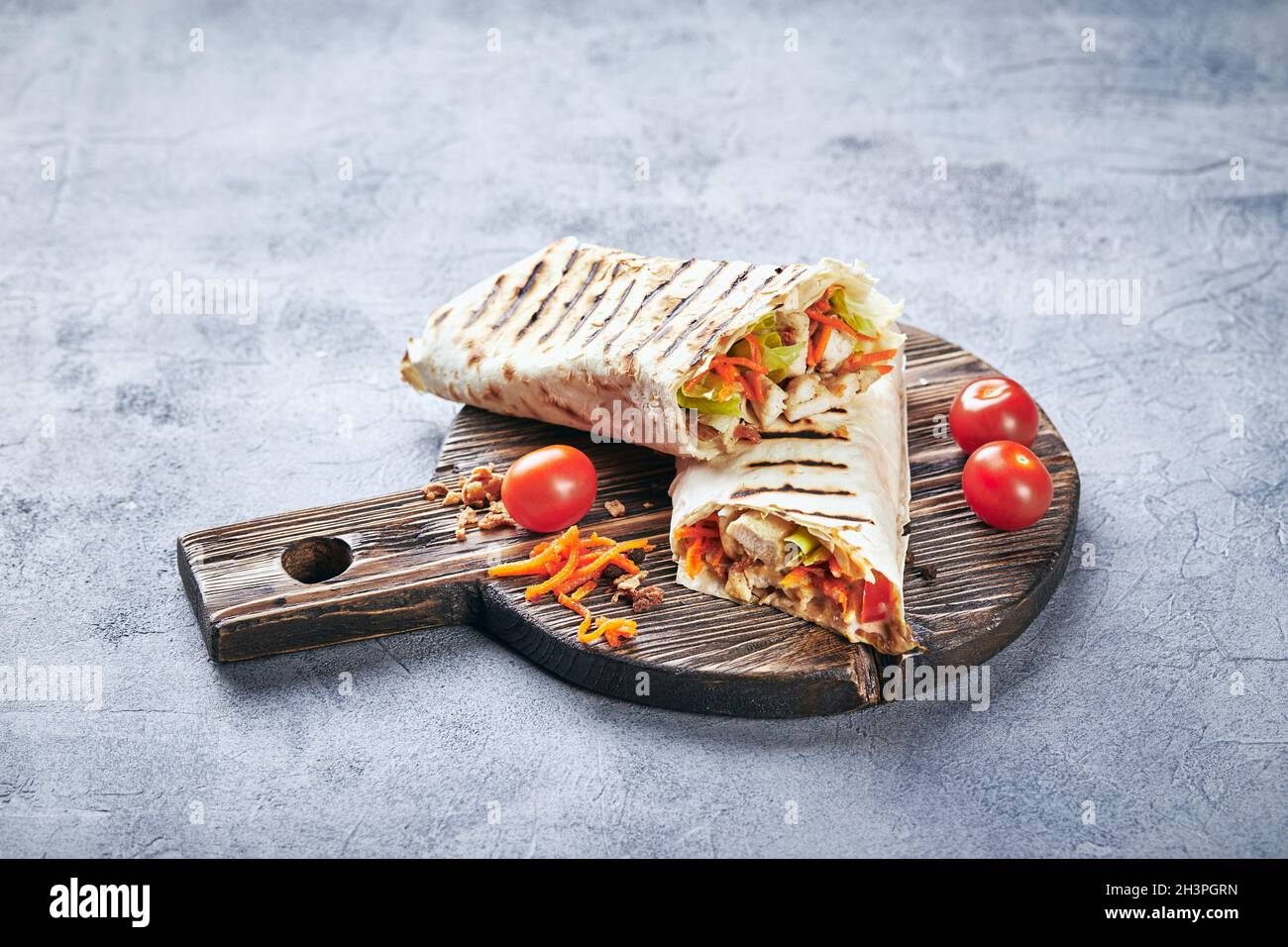 Eastern traditional shawarma with chicken and vegetables, Doner Kebab with sauces on wooden cutting board. Stock Photo