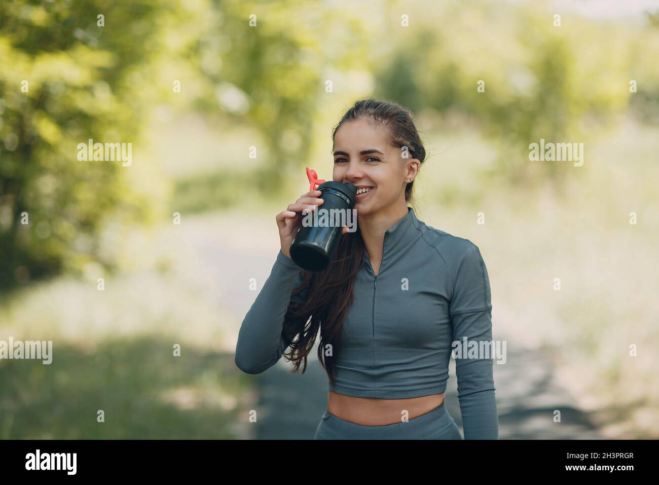 Tired runner woman jogger drinking bottled water after jogging in park outdoor. Stock Photo