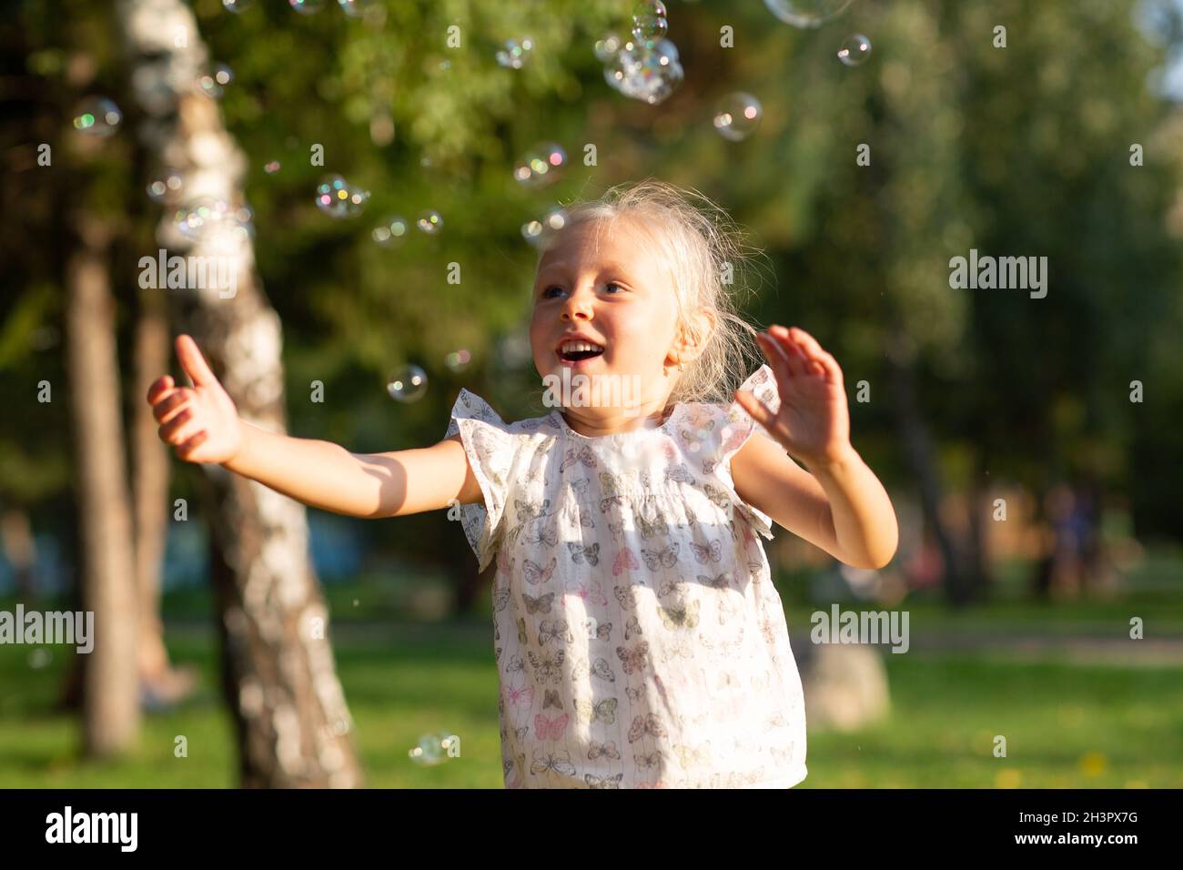 Little cute girl in the summer park blowing bubbles and having fun Stock Photo