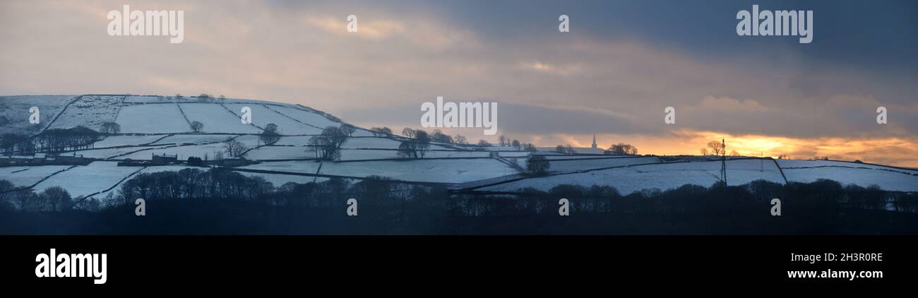 Panoramic view of a glowing orange sunset in a cloudy twilight winter sky with snow covered fields with stoodley pike monument i Stock Photo