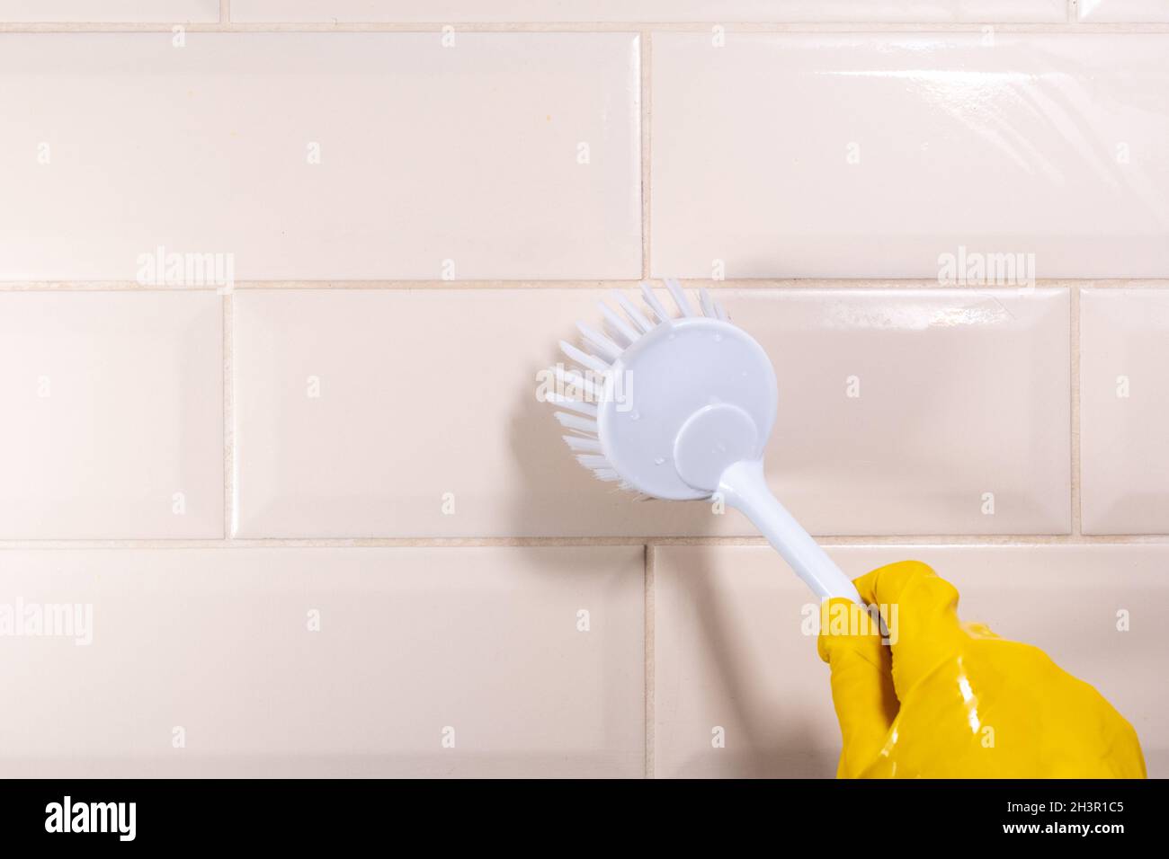 Hand in a yellow rubber glove wiping the ceramic tile surface with a ...