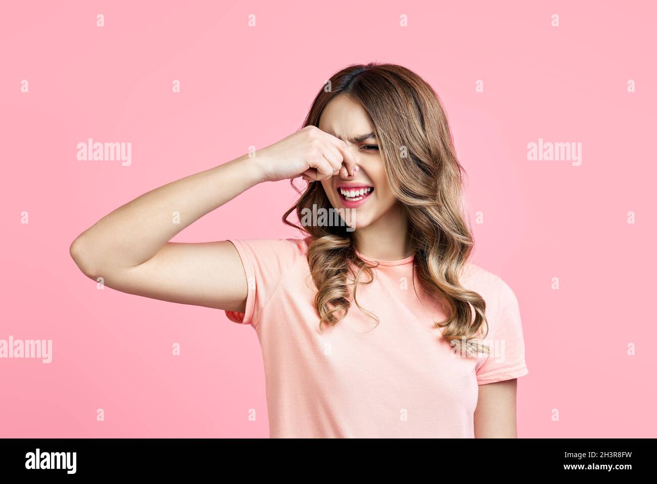 Smells bad, woman pinching nose with disgust on pink background Stock