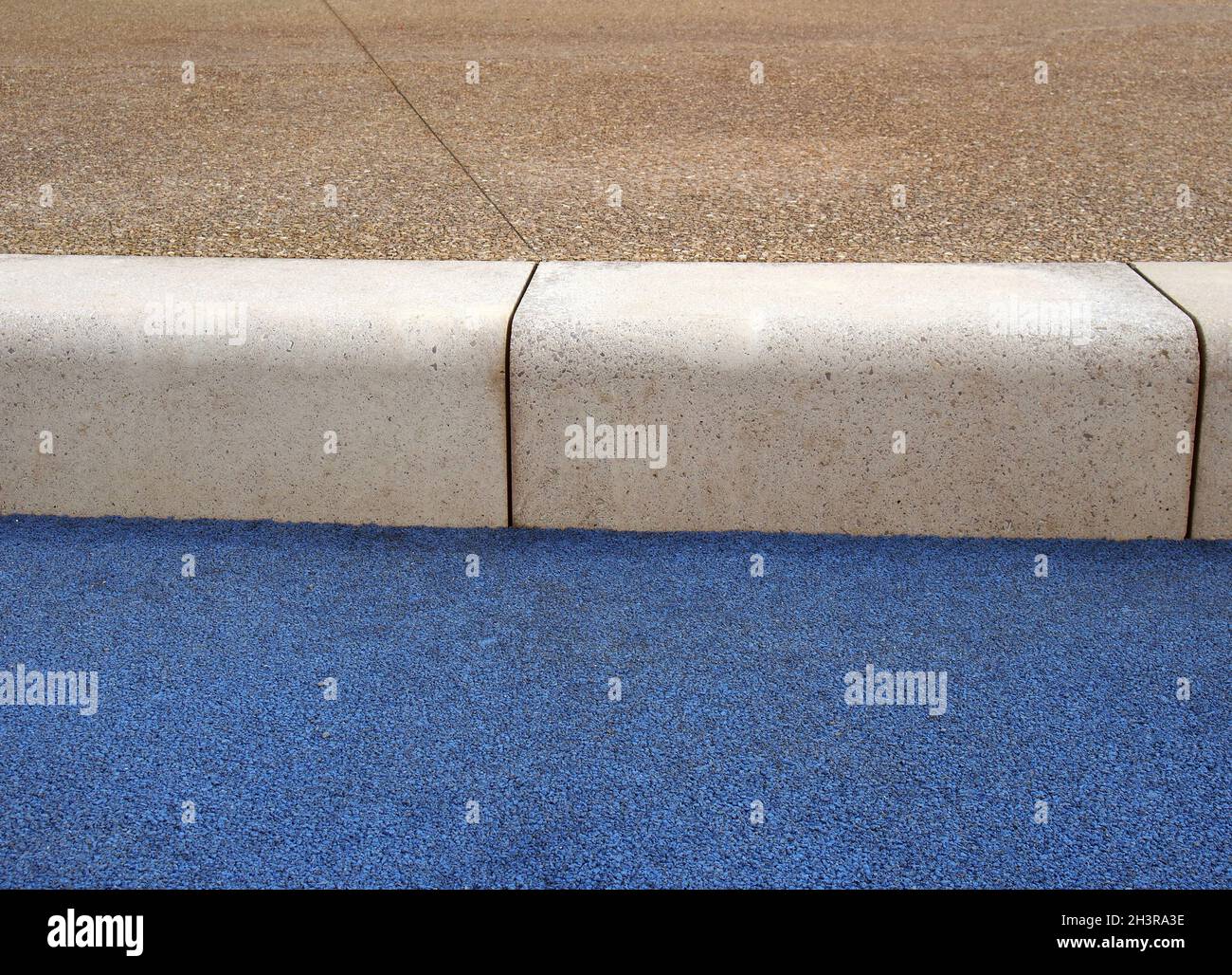 Close up of a concrete kerb and pavement with a blue asphalt road surface Stock Photo