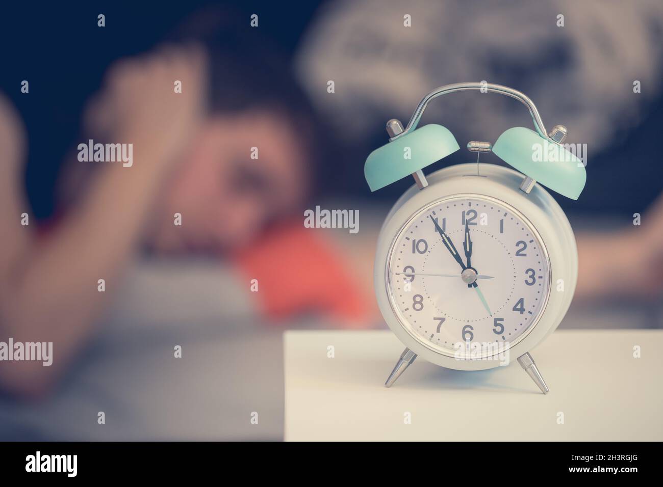 Alarm clock in the morning. Young man tries to sleep in the blurry