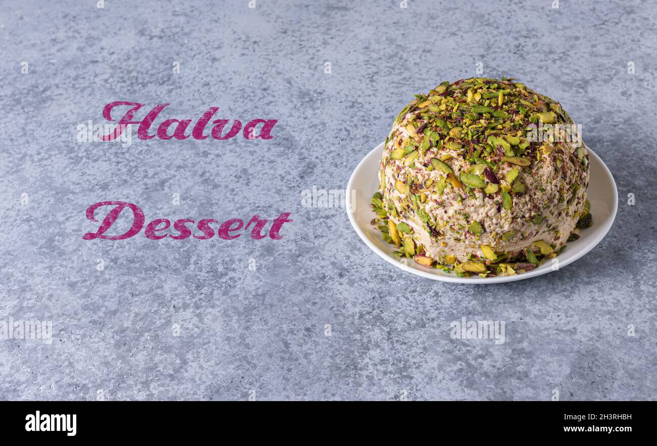 Sesame halva with chopped pistachios on white plate on gray stone background with Halva dessert pink text. Traditional middle eastern sweets. Jewish, Stock Photo