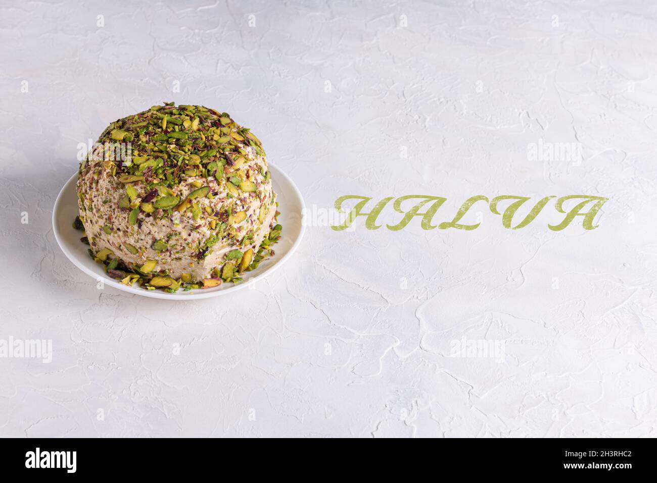 Sesame halva with chopped pistachios on white plate on textured background with Halva green text. Traditional middle eastern sweets. Jewish, turkish, Stock Photo