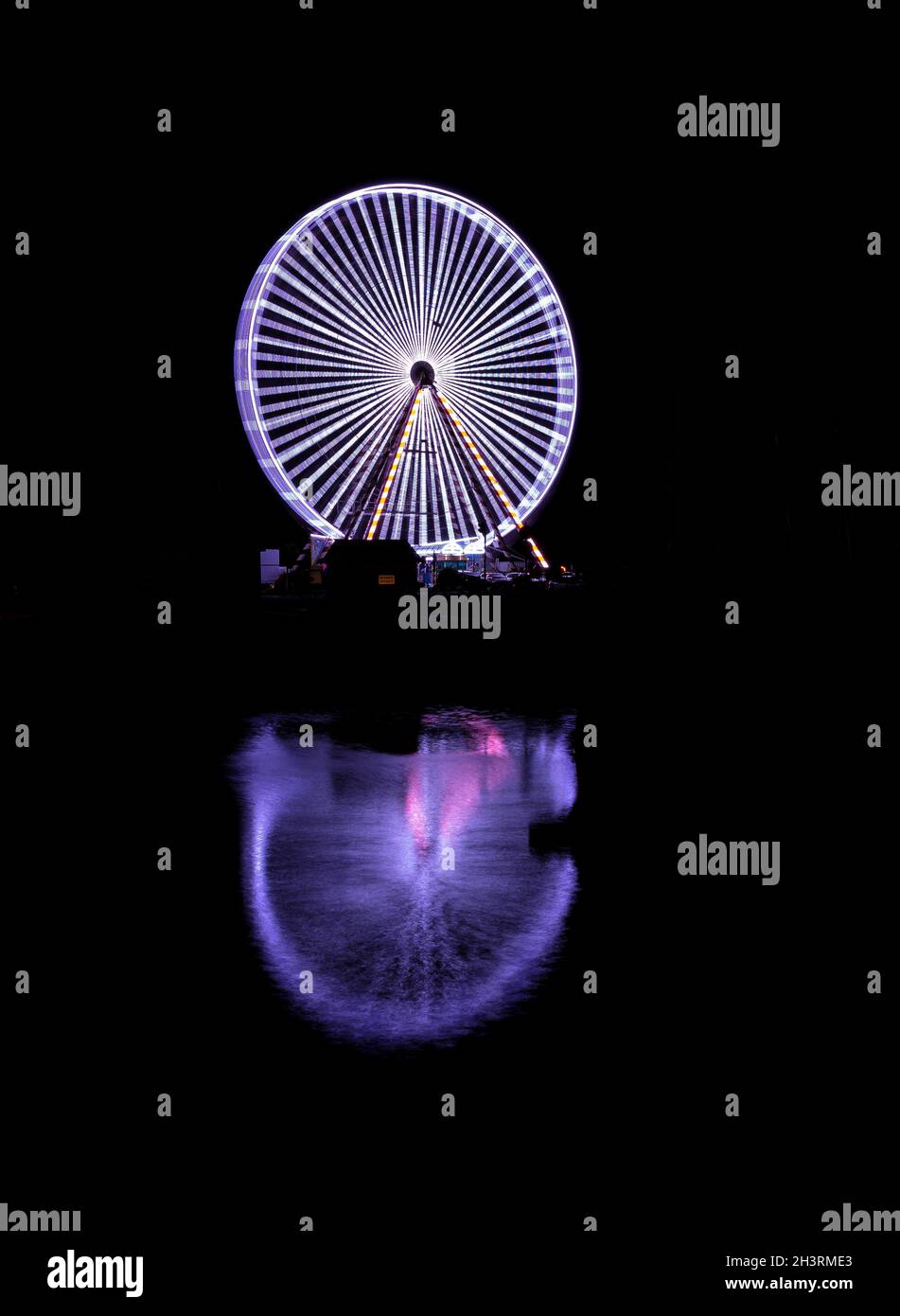 Spinning ferris wheel in Honfleur in the night with its reflection in the sea water Stock Photo