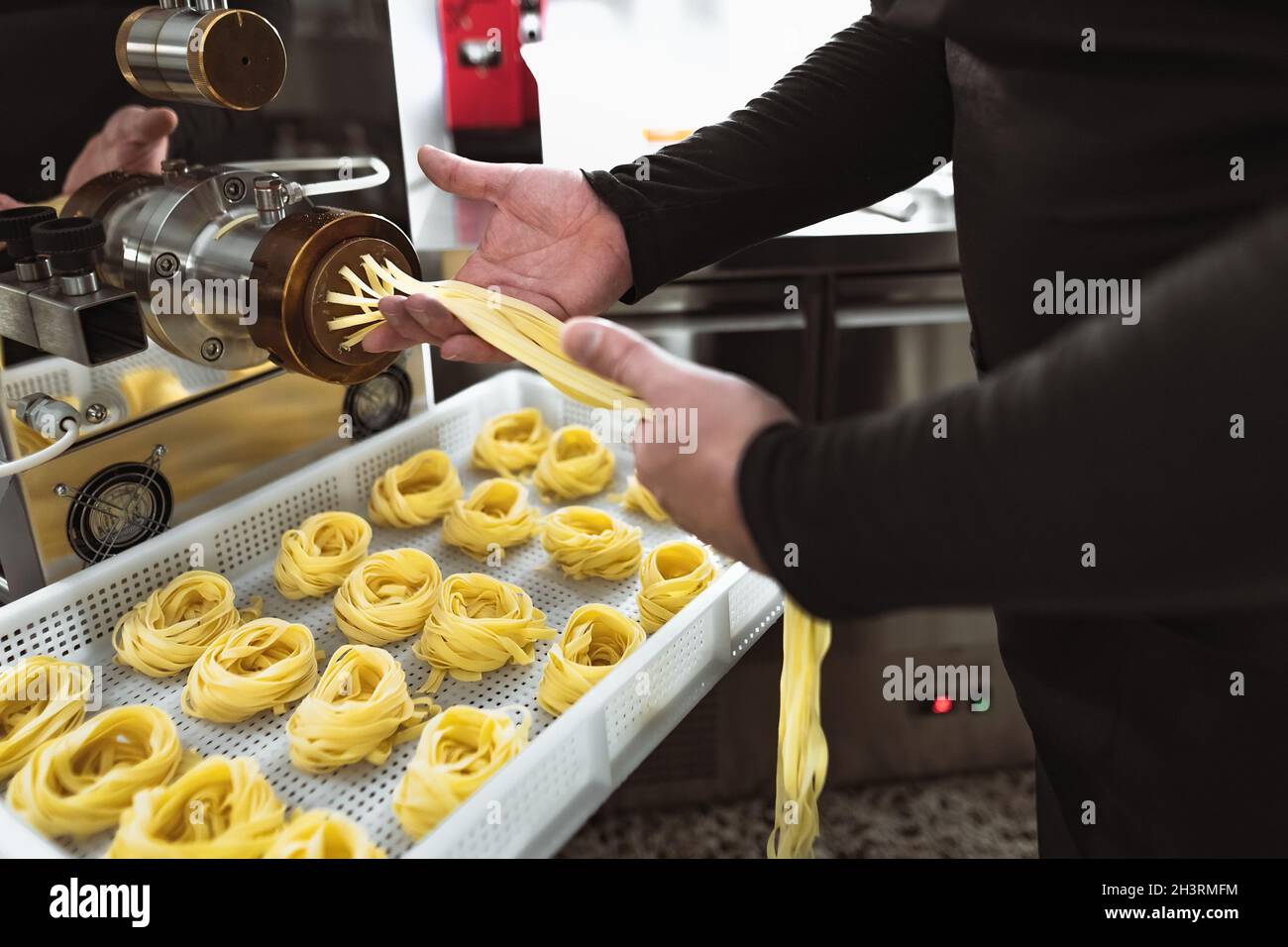 Close up male hands preparing fresh fettucine using machine inside pasta factory Stock Photo