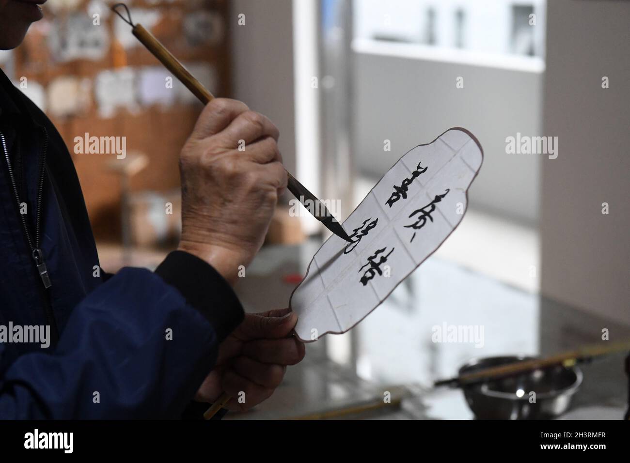 Lingchuan, China. 29th Oct, 2021. (211030) -- LINGCHUAN, Oct. 30, 2021 (Xinhua) -- Huang Shuofu, an inheritor of Guilin bamboo circular fan making technique, writes on a fan in Dingjiang Township of Guilin, south China's Guangxi Zhuang Autonomous Region, Oct. 29, 2021. Making of such a fan is not a simple task, craftsmen cut the soaked bamboo into dozens of strips to make fan frame, paste the surface with Xuan paper, cotton cloth and silk, finally make the circular fan through cutting and edge wrapping, and a good painting and/or calligraphic writing makes it a popular item in the cultural mar Stock Photo