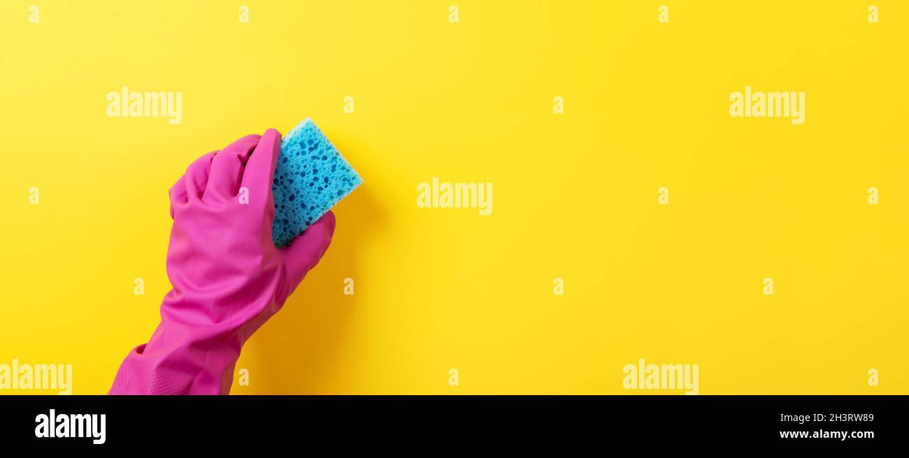 A hand in a pink rubber glove holds a blue washing sponge over yellow ...