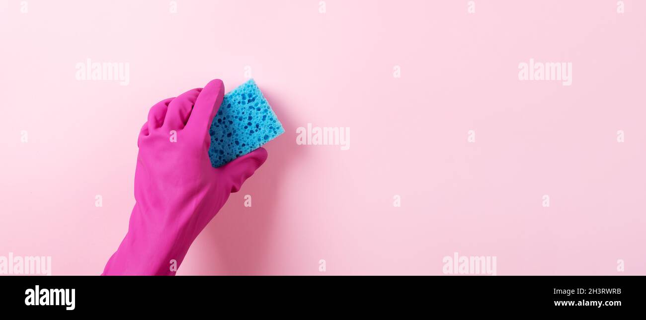 A hand in a pink rubber glove holds a blue washing sponge over pink ...