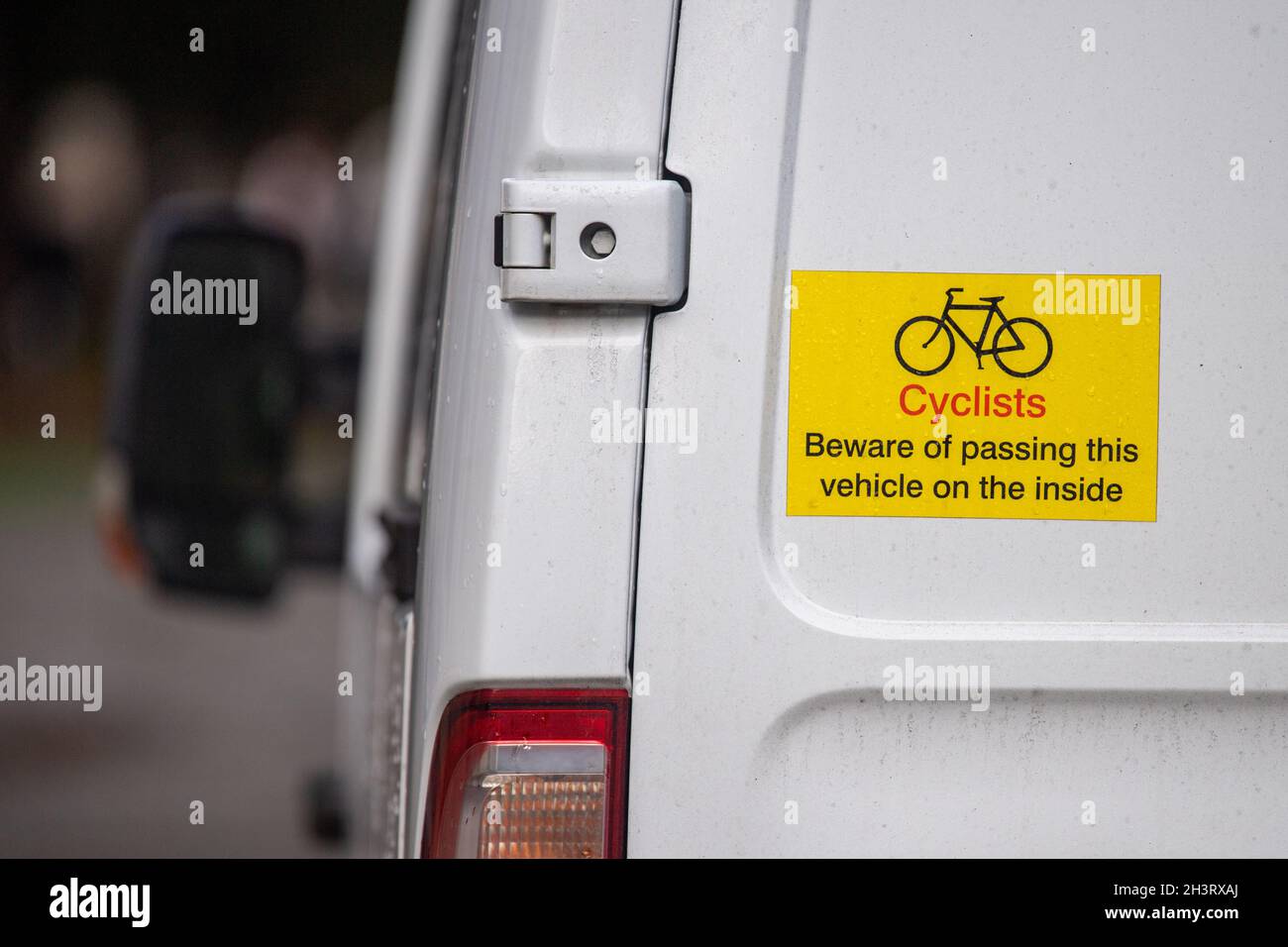 A yellow sign on the rear of a white van warning cyclists of the dangers of passing the vehicle Stock Photo