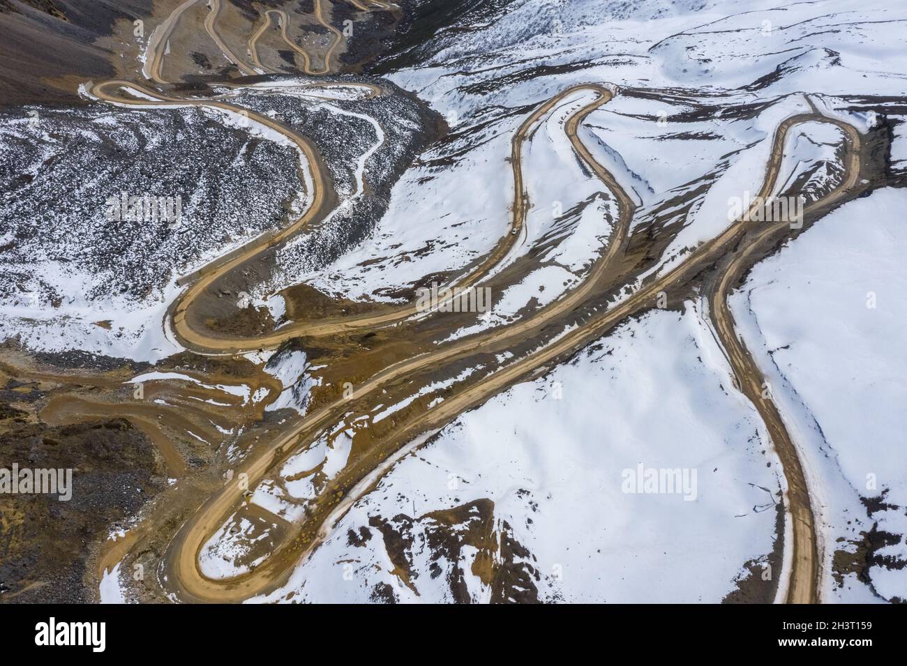 Aerial view of the winding dirt road on snow mountain Stock Photo