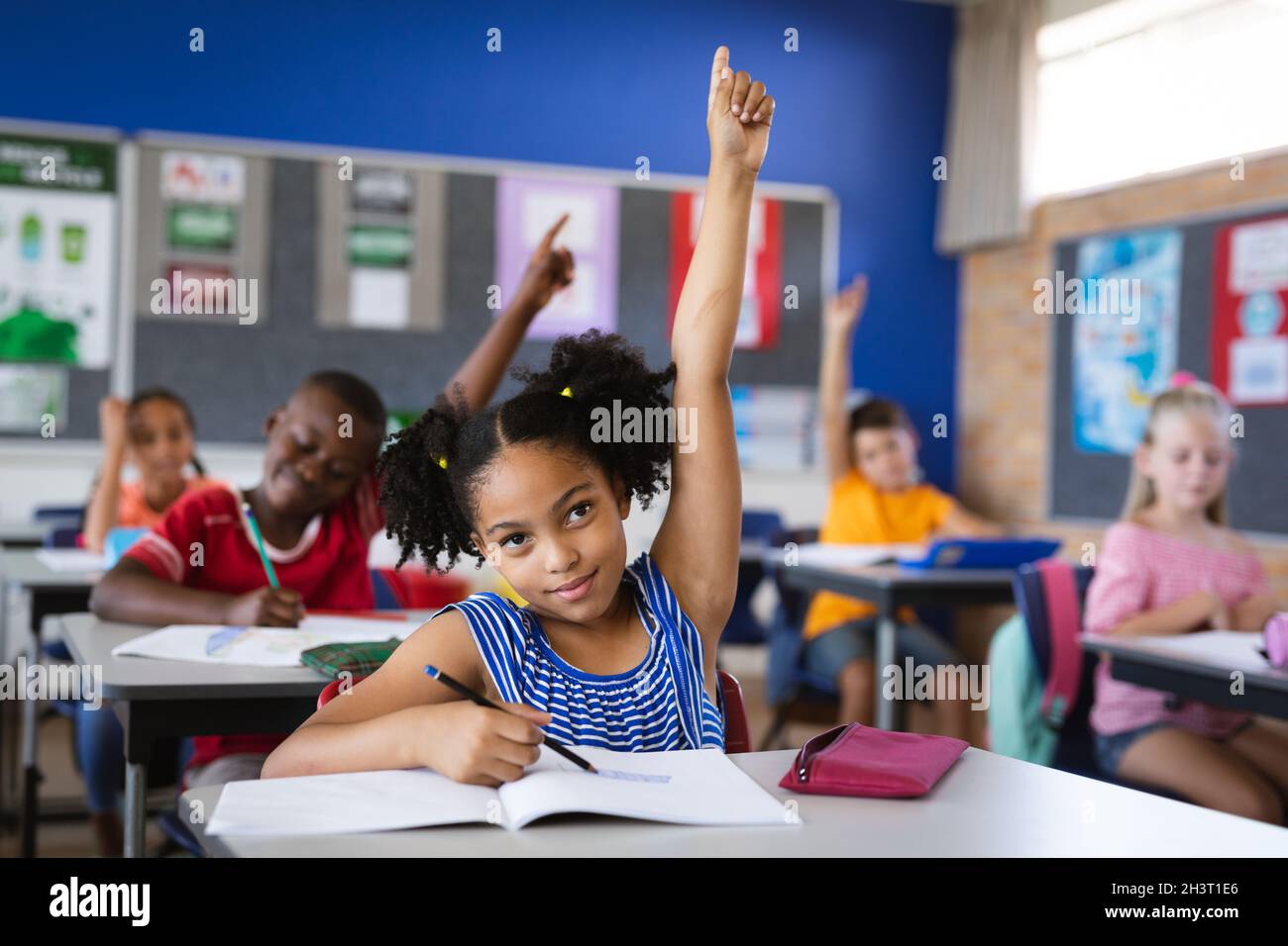 African american girl raising her hands while sitting on her desk in ...