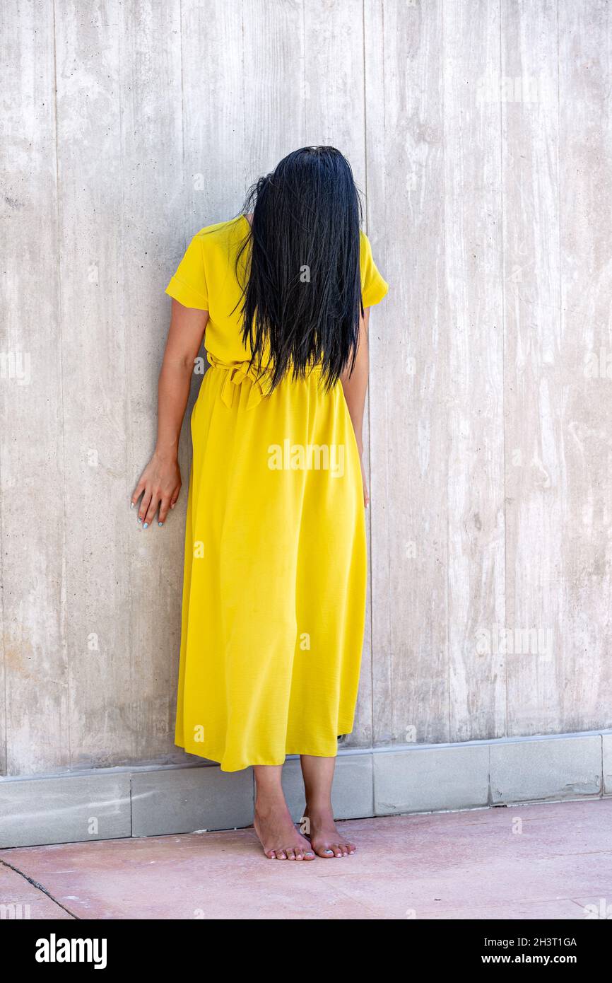 Vertical image of an adult woman with long black hair barefoot and standing  leaning on a wall with her head tilted forward and her hair covering her f  Stock Photo - Alamy