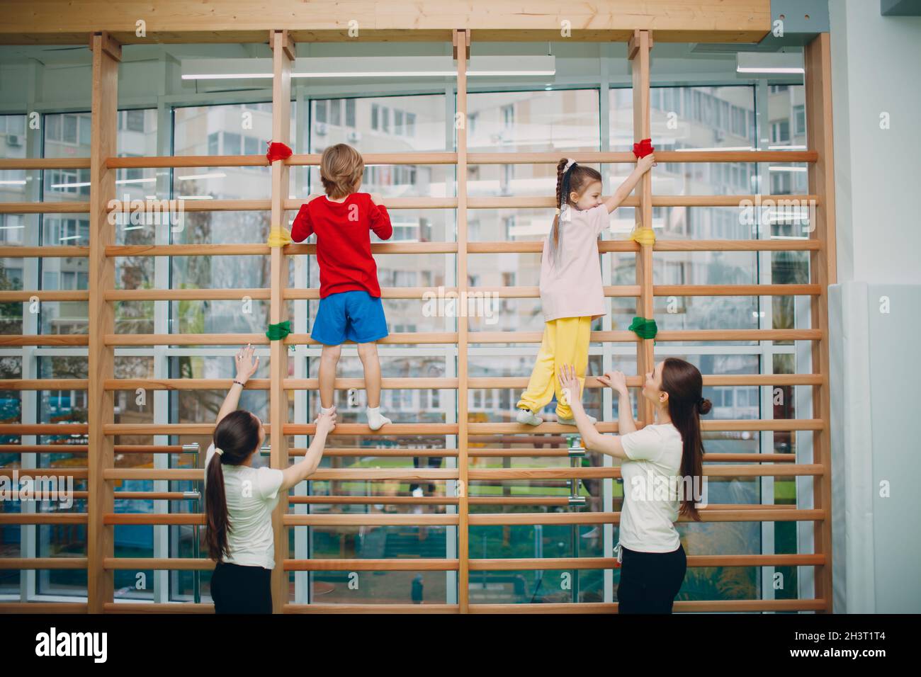 Kids at Swedish wall exercises in gym at kindergarten or elementary school with teachers. Children sport and fitness concept. Stock Photo