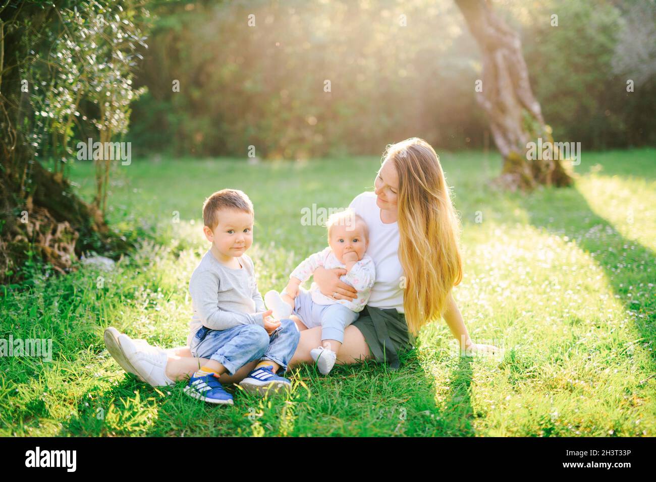 Mother is sitting on the lawn with her two children Stock Photo