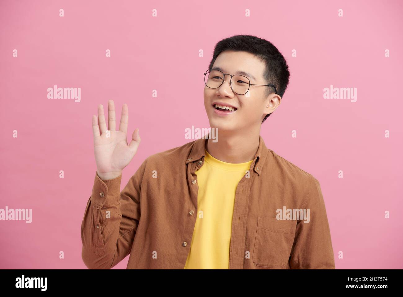 Asian happy young handsome man in casual clothing waving hand greeting say hello hi of goodbye on pink background. Stock Photo